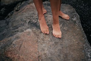 Close-up of bare feet standing on a large rock surface outdoors, capturing a natural and earthy vibe.