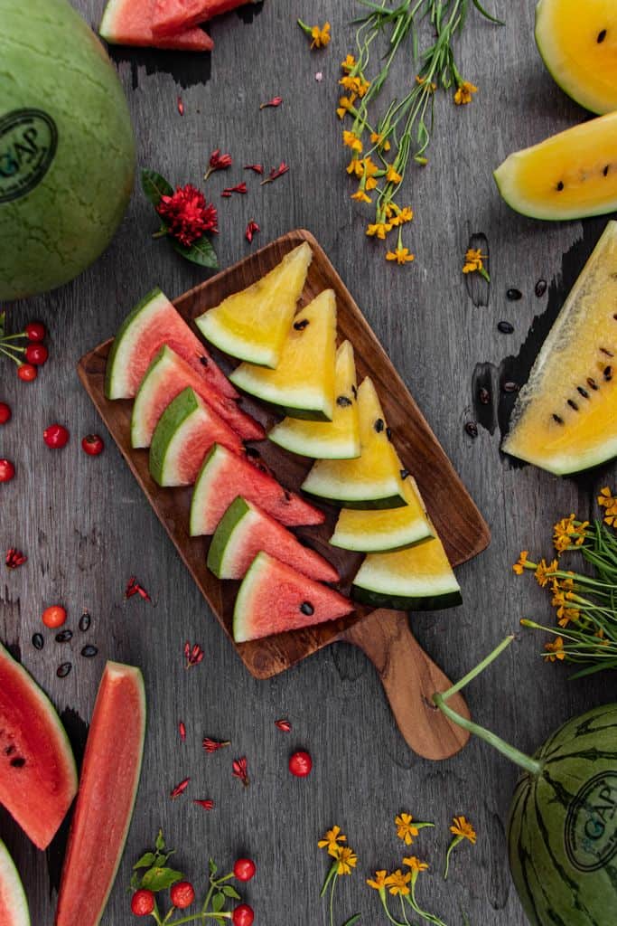 Top view of sliced red and yellow watermelons on wooden surface with flowers.